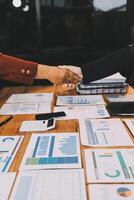 Two business people shaking hands over a table with papers and other documents photo