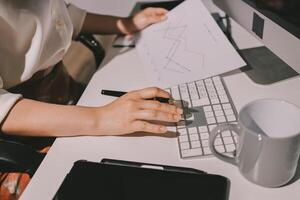 A woman is working on her computer with a pen and paper photo