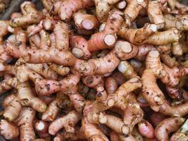 A large pile of fresh turmeric roots with rough brown skin and visible orange flesh in a market stall. photo
