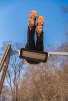 Child swinging upside down on swing seat in park, view from below, sunny winter day photo