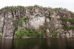 Steep fjord cliff face with green forest reflection near Bergen, Norway photo