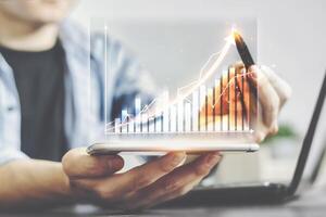 Business men use the pen to point at the graph of business growth, positive value increases. The business graph shown in a virtual screen on a smartphone, arrow the direction of growth and success. photo