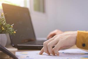Close up of hands typing on a laptop while reviewing business documents with graphs, illustrating work from home, data analysis, and planning. photo