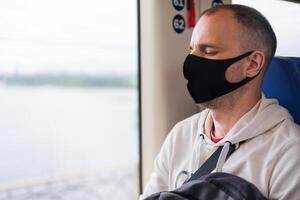 Traveler young man in a protective mask sleeps on the train by the window. Close-up. Copy space. photo