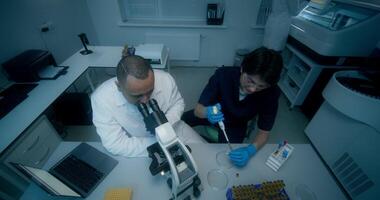 A man and a woman in lab coats are working in a medical laboratory, conducting a blood test and using a microscope. They are talking sitting at the table - sitting photo