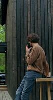 A man in casual clothes is talking on a mobile phone and drinking coffee standing on the terrace of a stylish cottage on a summer day. photo