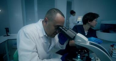 A man and a woman in lab coats are working in a medical laboratory, conducting a blood test and using a microscope. They are talking sitting at the table - talking photo
