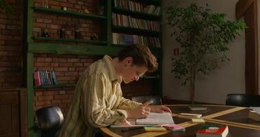 A man is studying the Bible while sitting at a table indoors. He prays with his hands folded in front of him. Daylight photo