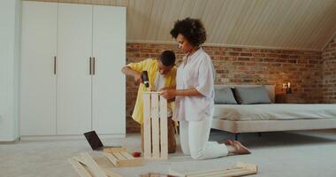 Mom and son make wooden furniture using a drill, sitting on the floor in front of an open laptop at home - sitting photo