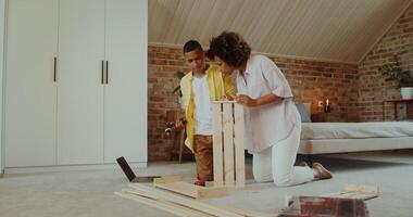 Mom and son make wooden furniture using a drill, sitting on the floor in front of an open laptop at home photo