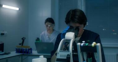 Two women in medical clothes work in a medical laboratory, using a microscope photo