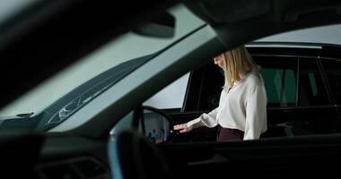 A stylish woman chooses a car by walking around the showroom of a car dealership with a thoughtful look and looking into cars - walking photo