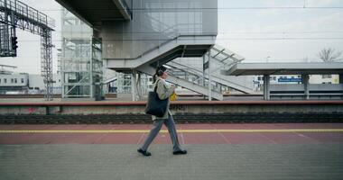 A woman in formal clothes and with headphones on her head uses a mobile phone walking along the railway platform - headphones photo
