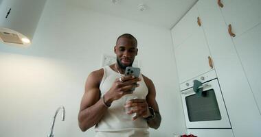 A man in pajamas uses a mobile phone and drinks water standing in the kitchen at home. Daylight - standing photo