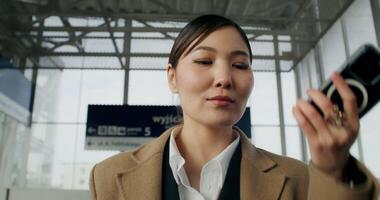 A woman in formal clothes records a voice message on a mobile phone walking through a railway station photo