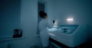 Work in a medical laboratory. A woman in a lab coat, disposable gloves and safety glasses sets up a blood splitting device using a screen photo
