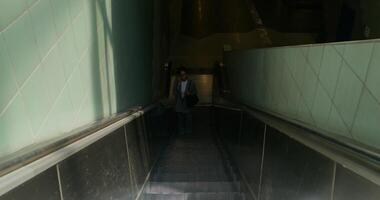 A woman in formal clothes is talking on a mobile phone. She rides the escalator coming up from the subway station - escalator photo