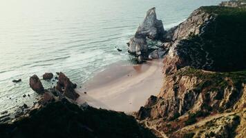 The drone flies over the top of a grassy mountain overlooking the sea, with a sandy beach between the rocks - overlooking photo