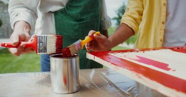 A man in an apron and a boy paint the door in red color while standing in the backyard. Close-up of hands, no face photo