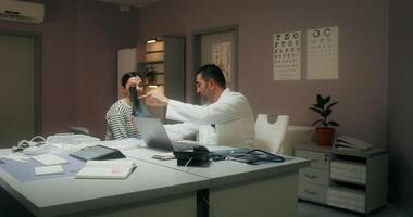 A doctor in a white coat shows a woman patient an X-ray, and then writes down appointments in a notebook, sitting at his desk in the medical office at the clinic - writes photo