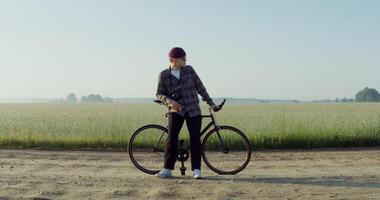 A young man with a camera around his neck stopped near a wheat field, resting after cycling and admiring the beauty of nature in the rays of the rising sun. 4k , red komodo photo