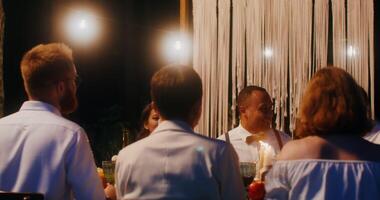 The bride and groom kiss standing up from behind the covered festive table, at which the guests are sitting - covered photo