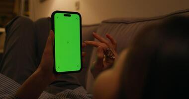 A woman uses a mobile phone with a green screen lying on the couch at home, an unrecognizable person - unrecognizable photo