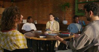 Bible Study Group. Young people talk in pairs while sitting at a table indoors. The books are on the table. Daylight - Daylight photo