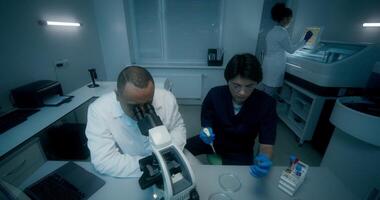 A man and a woman in lab coats are working in a medical laboratory, conducting a blood test and using a microscope. They are talking sitting at the table - conducting photo