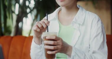 A young woman drinks ice coffee from a straw, sitting at a table opposite an open laptop in a cafe, cheesecakes are on the table photo