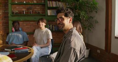 A group of young people are smiling and talking while sitting around a table. They study the Bible together. Daylight photo