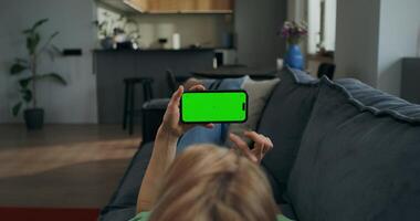A woman holds a mobile phone with a green screen horizontally in her hands watching , rear view, an unrecognizable person photo