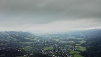 Vertical panning from a drone, a view of mountain valley with city in a lowland at foot of gently sloping mountains overgrown with a spruce forest, on a cloudy day at dusk photo