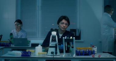A group of laboratory assistants in medical clothes work in a medical laboratory, using a microscope and conducting a blood test - medical - of photo