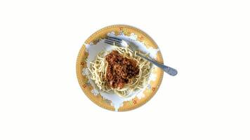 Top view of spaghetti with meat sauce served on a floral-patterned plate, accompanied by a fork and spoon, isolated on a clean white background. video