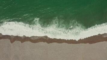 Top view of the sea shore. Emerald water with foam washes a shallow pebble beach, drone . photo