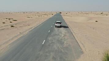 The car drives along an asphalt road in the desert, leaving behind a sandy dust. Drone photo