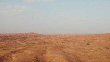 Drone view of a lifeless desert with sparse vegetation among red sand. Cars drive into a sandy mountain in the background photo