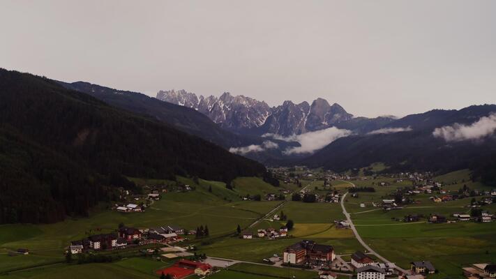 Dramatic drone view of a mountain valley with a village in a lowland with low hanging clouds covering the mountain tops. Austria, Alps filming at dusk - valley