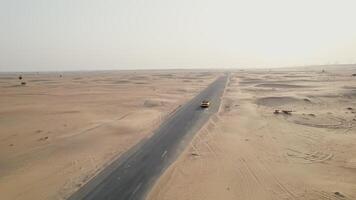 A yellow car is driving along an asphalt road in the desert, raising sand dust behind it. Drone - asphalt photo