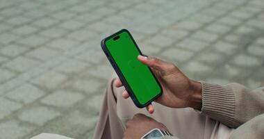 A man uses a mobile phone with a green screen sitting outdoors, close-up of his hands, an unrecognizable person - screen photo