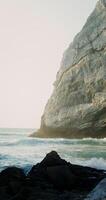 A cliff on the seashore, sea waves beating against a stone - against photo