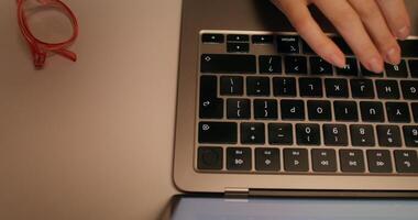 A woman typing on a laptop keyboard sitting at a table indoors, close-up of her hands, top view, unrecognizable person photo