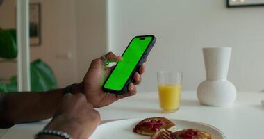A man uses a mobile phone with a green screen during breakfast at home. Close-up of his hand, an unrecognizable person photo