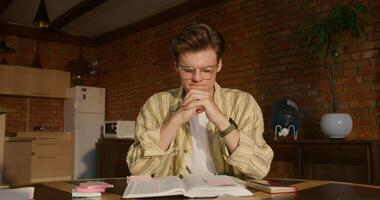 A man is studying the Bible while sitting at a table indoors. He prays with his hands folded in front of him. Daylight - folded photo
