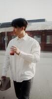 A young man with a paper bag in his hands drinks juice from a disposable cup with a straw while walking around the city - around photo