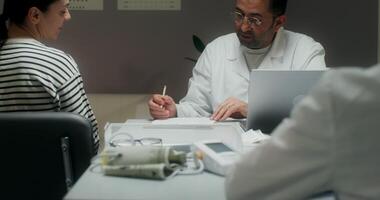 The doctor listens to the patient's complaints sitting in front of an open laptop at the table and writes in a notebook. Medical appointment at the clinic - complaints photo
