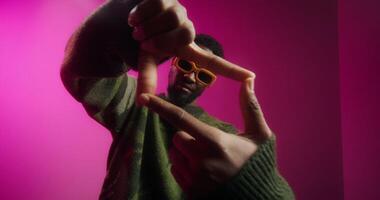 A bearded man in yellow sunglasses and a sweater poses standing on a pink background in a studio in the studio - sunglasses photo