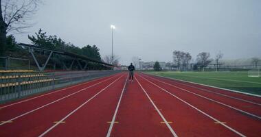 A man in sports clothes runs around the stadium on a cold day alone, front view - stadium photo