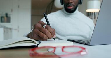 A man with headphones is talking on a chat on a laptop, sitting at a table at home. He writes in a notebook. Remote work - sitting photo